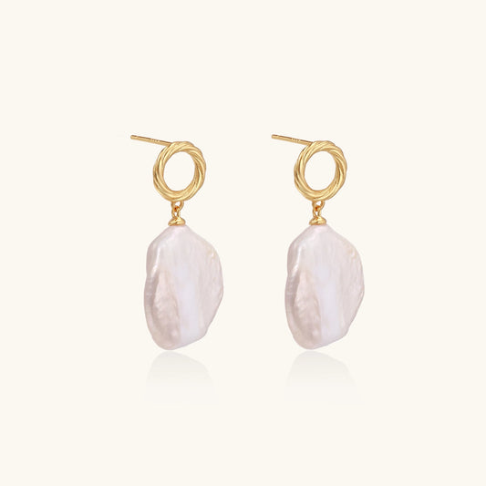Gold-plated twisted stud earrings with large blush baroque pearls hanging elegantly on white background.