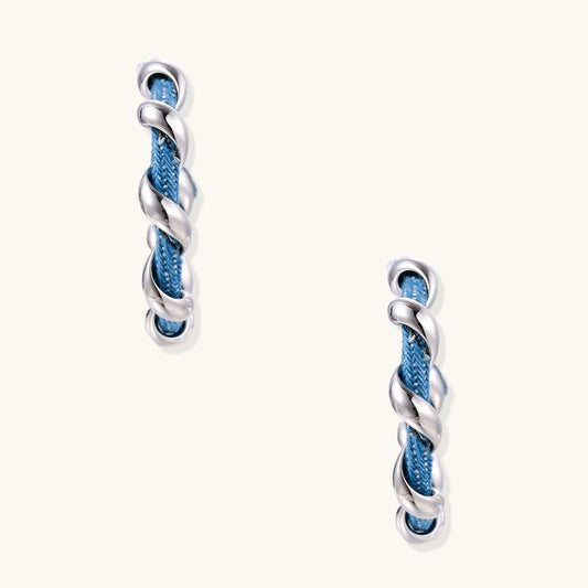 Twisted hoop earrings featuring blue denim fabric braided with gold-plated metal in a spiral design on white background.