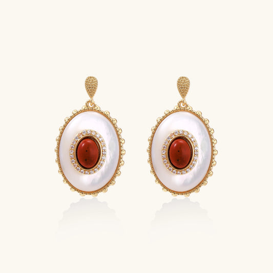 Gold-plated drop earrings with oval mother-of-pearl stones, central red gemstones, and crystal accents on white background.