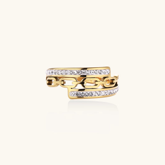 Gold-plated chain-link ring with rhinestone rows on cream background, showing bold geometric design and sparkling details.