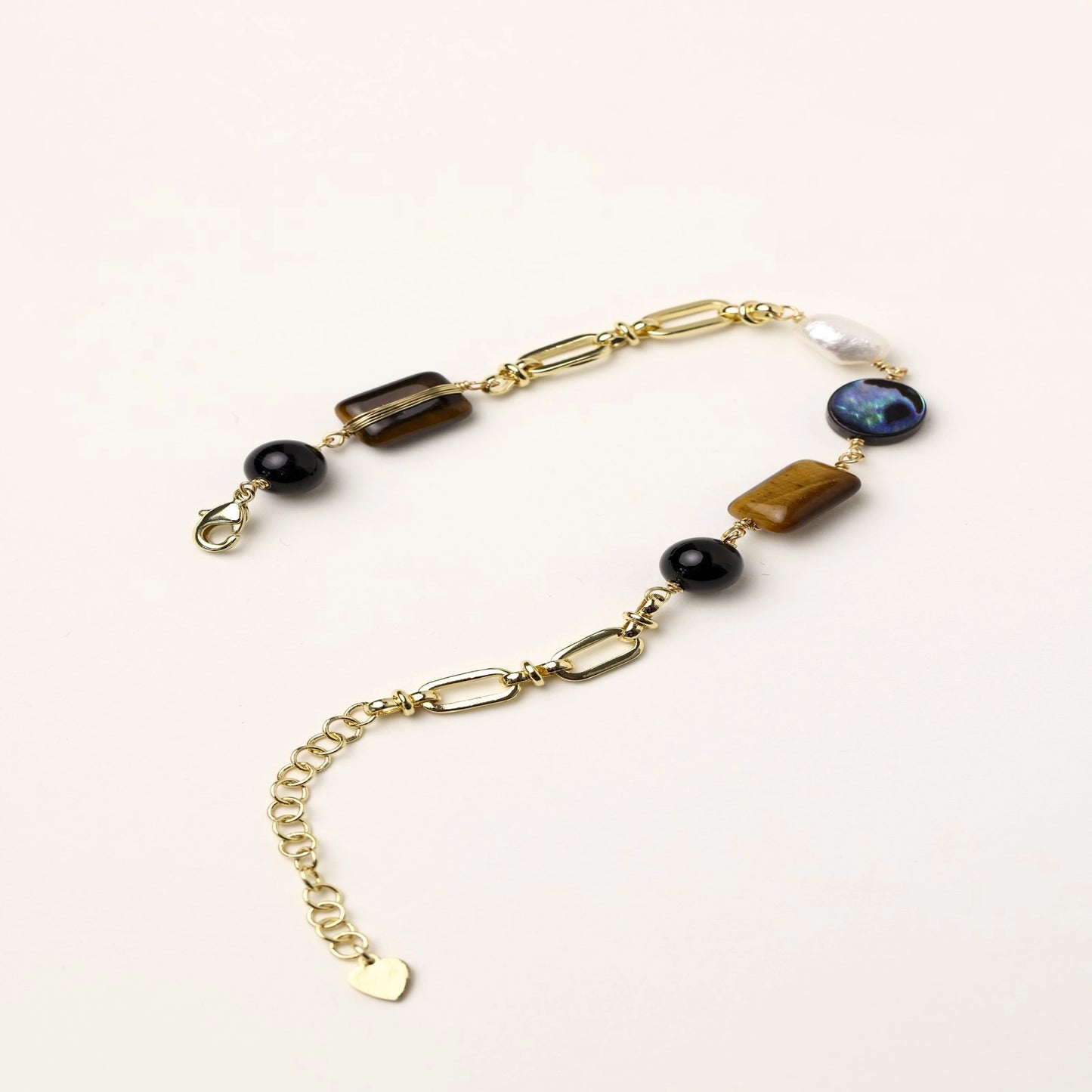 Gold-plated chain bracelet featuring tiger's eye, obsidian, freshwater pearls and abalone shell on white background