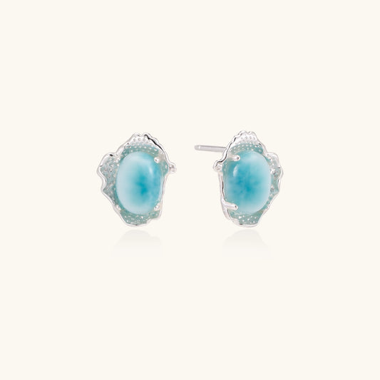Close-up of sterling silver stud earrings with oval larimar stones in flowing wave-like settings on white background.