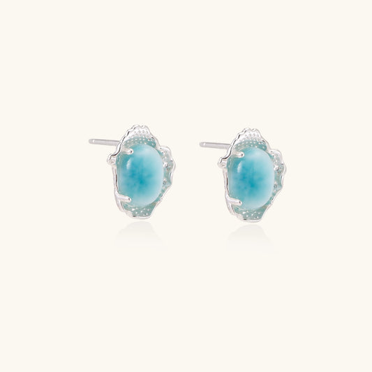 Close-up of sterling silver stud earrings with oval larimar stones in flowing wave-like settings on white background.