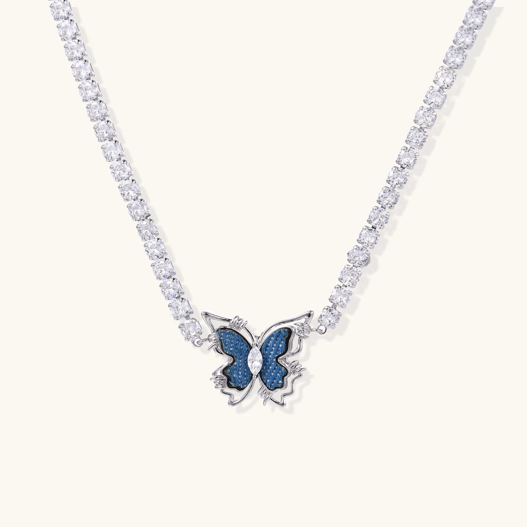 Gold-plated tennis chain necklace with blue denim butterfly pendant and zirconia stones on light background.