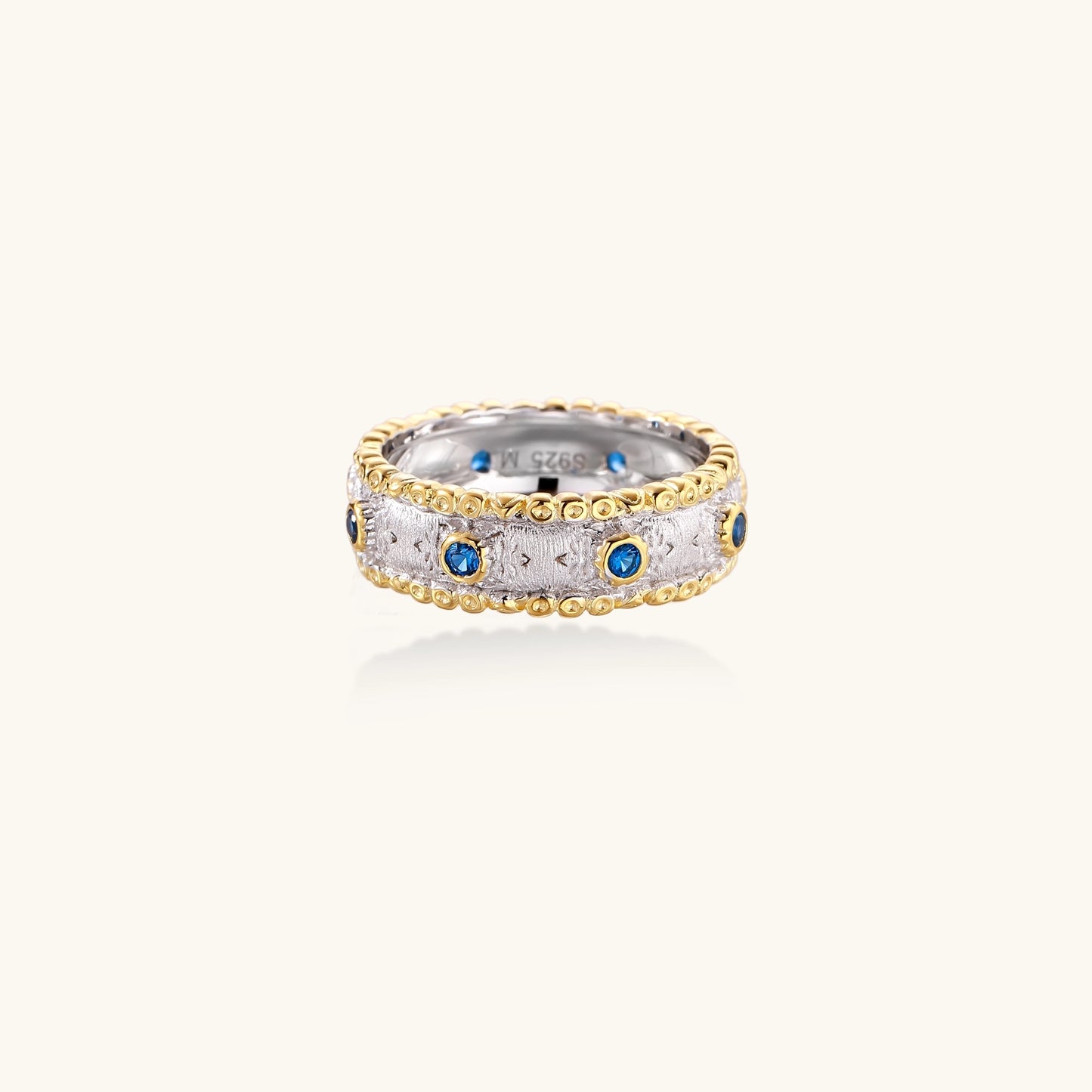 Sterling silver ring with brushed center band, blue zirconia stones, and 24k gold-plated decorative borders.