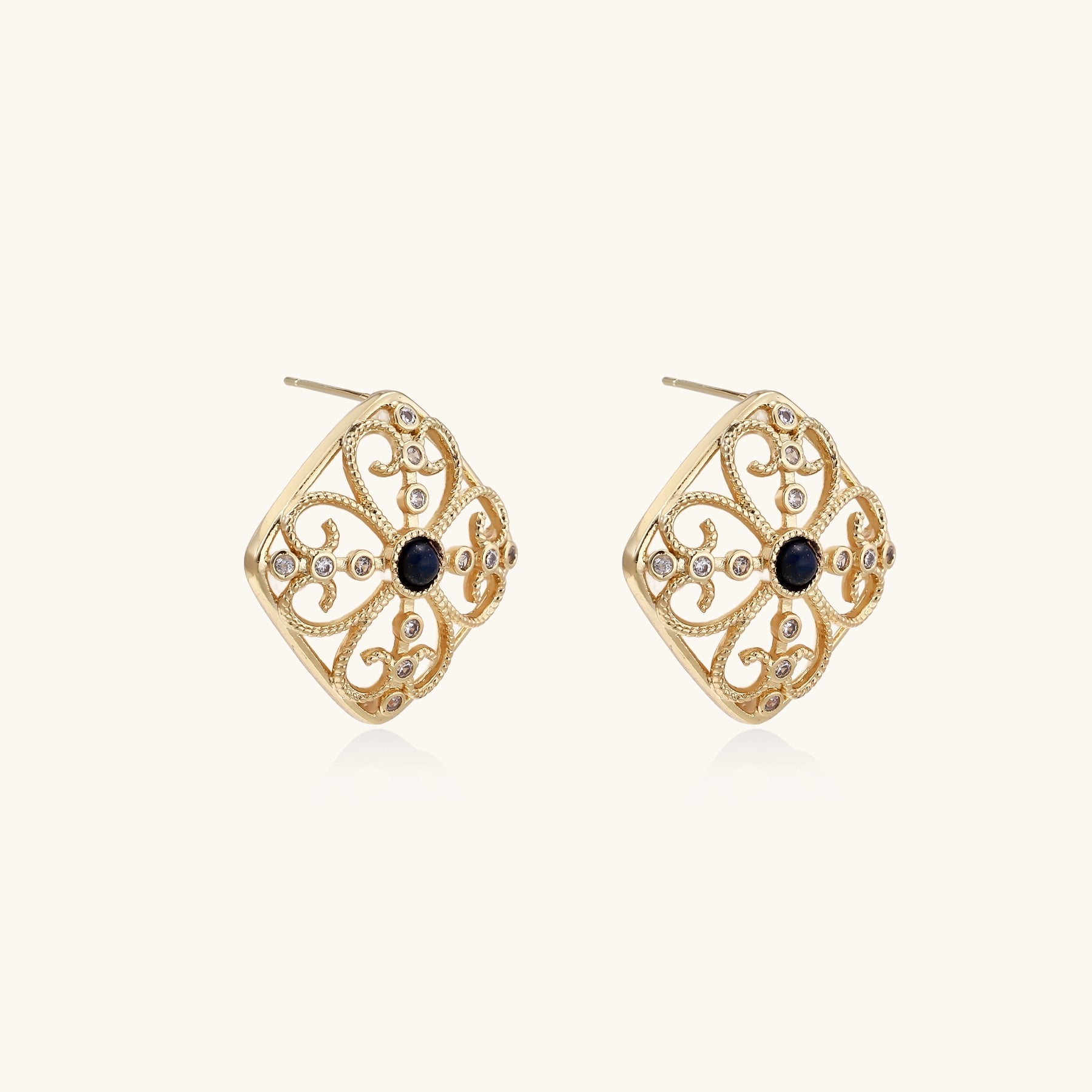 Ornate 18K gold plated stud earrings with intricate filigree design and central lapis lazuli stones on cream background.