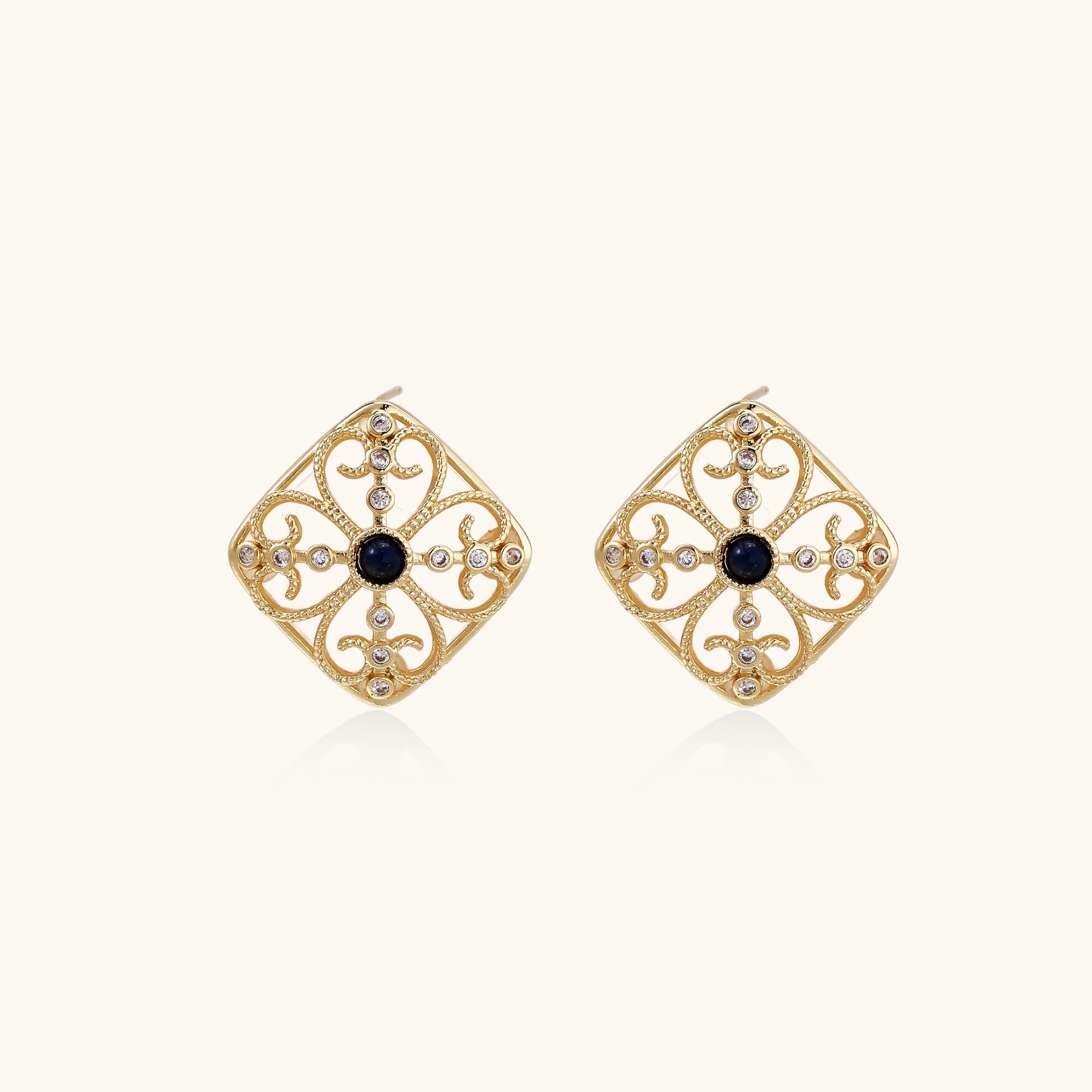 Ornate 18K gold plated stud earrings with intricate filigree design and central lapis lazuli stones on cream background.