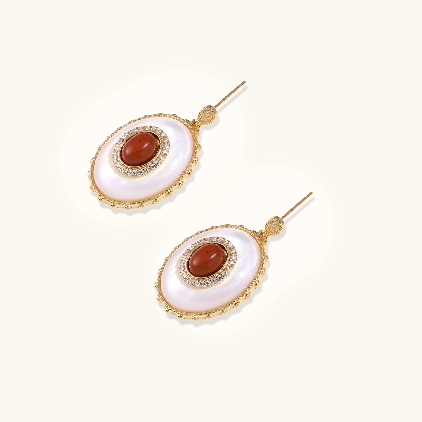 Gold-plated drop earrings with oval mother-of-pearl stones, central red gemstones, and crystal accents on white background.