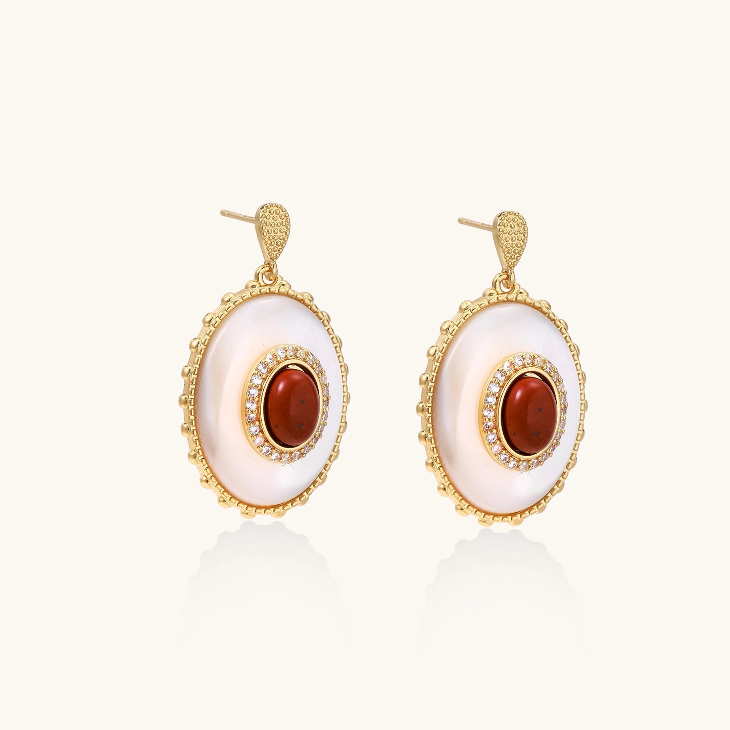 Gold-plated drop earrings with oval mother-of-pearl stones, central red gemstones, and crystal accents on white background.
