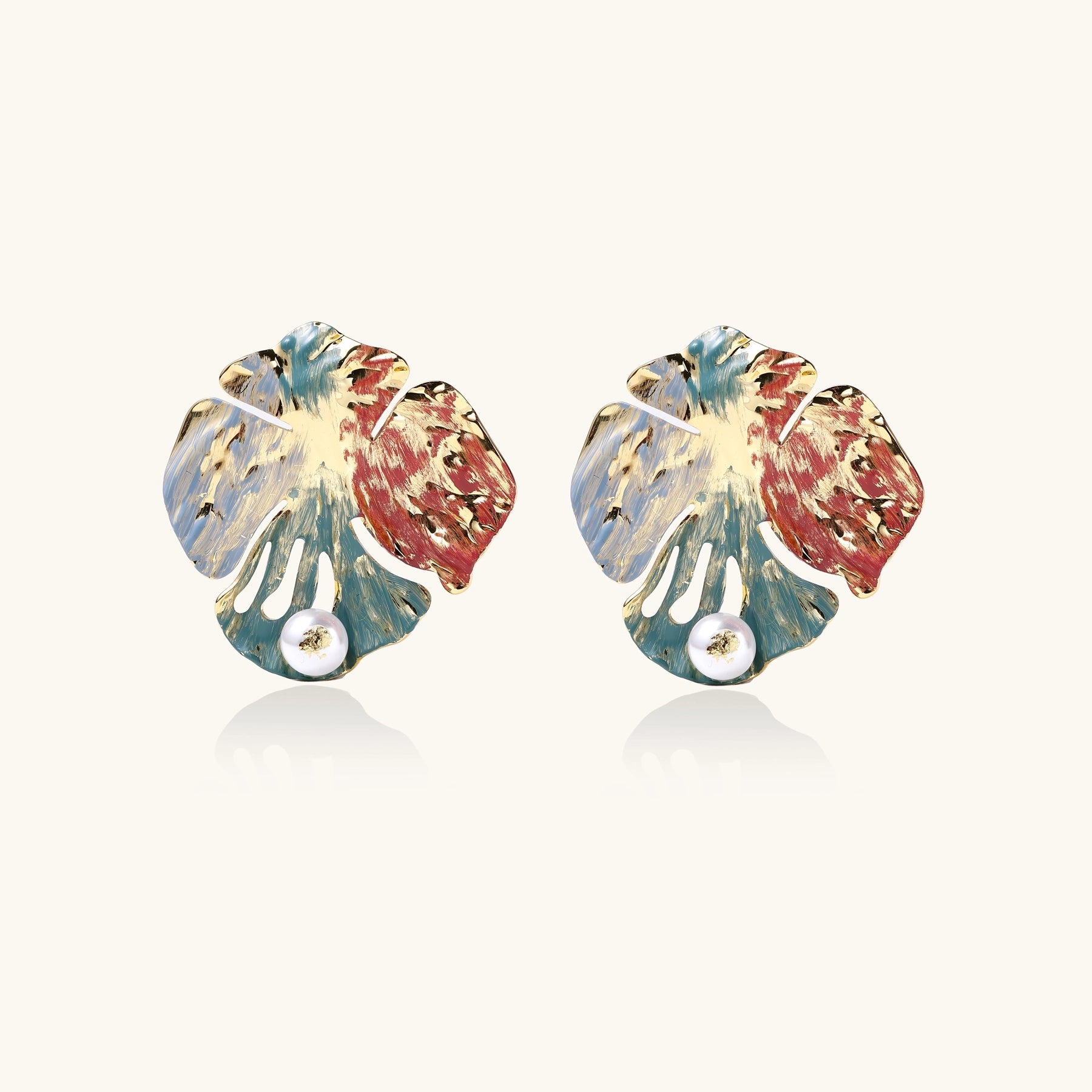 Colorful enamel monstera leaf earrings with pearl accents in teal, coral and gold tones on neutral background.