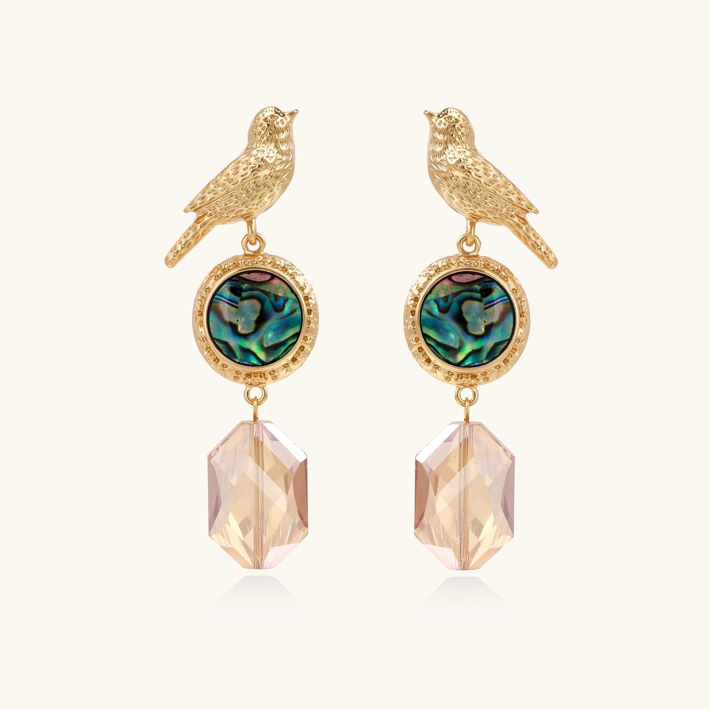 Gold-plated bird dangle earrings with iridescent abalone shell discs and champagne crystal drops on white background.