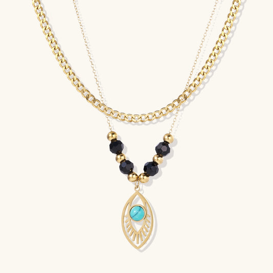Gold layered necklace set with evil eye pendant, turquoise center stone, and black beaded chain on cream background
